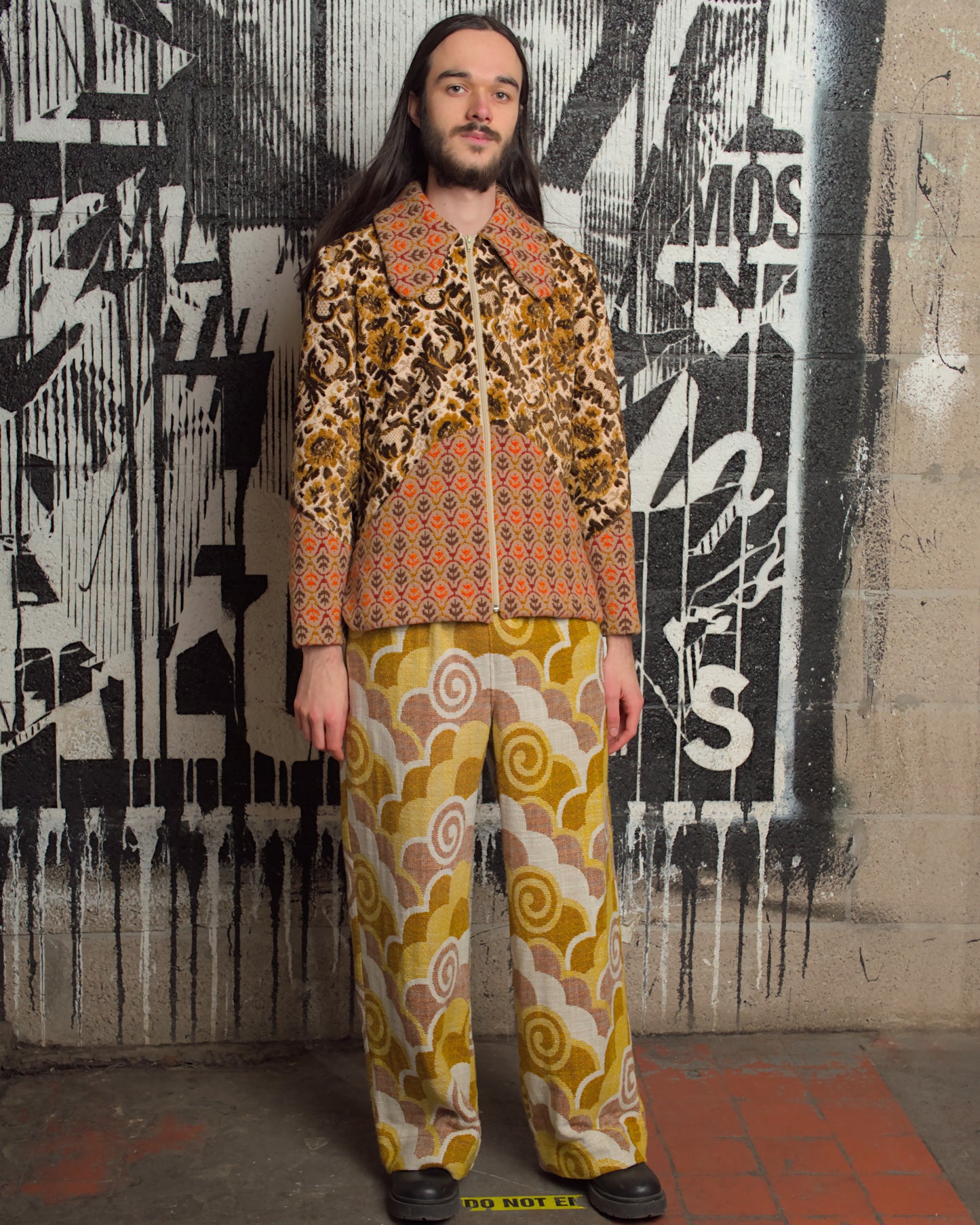 Person wearing a patterned outfit in front of a graffiti-covered wall.