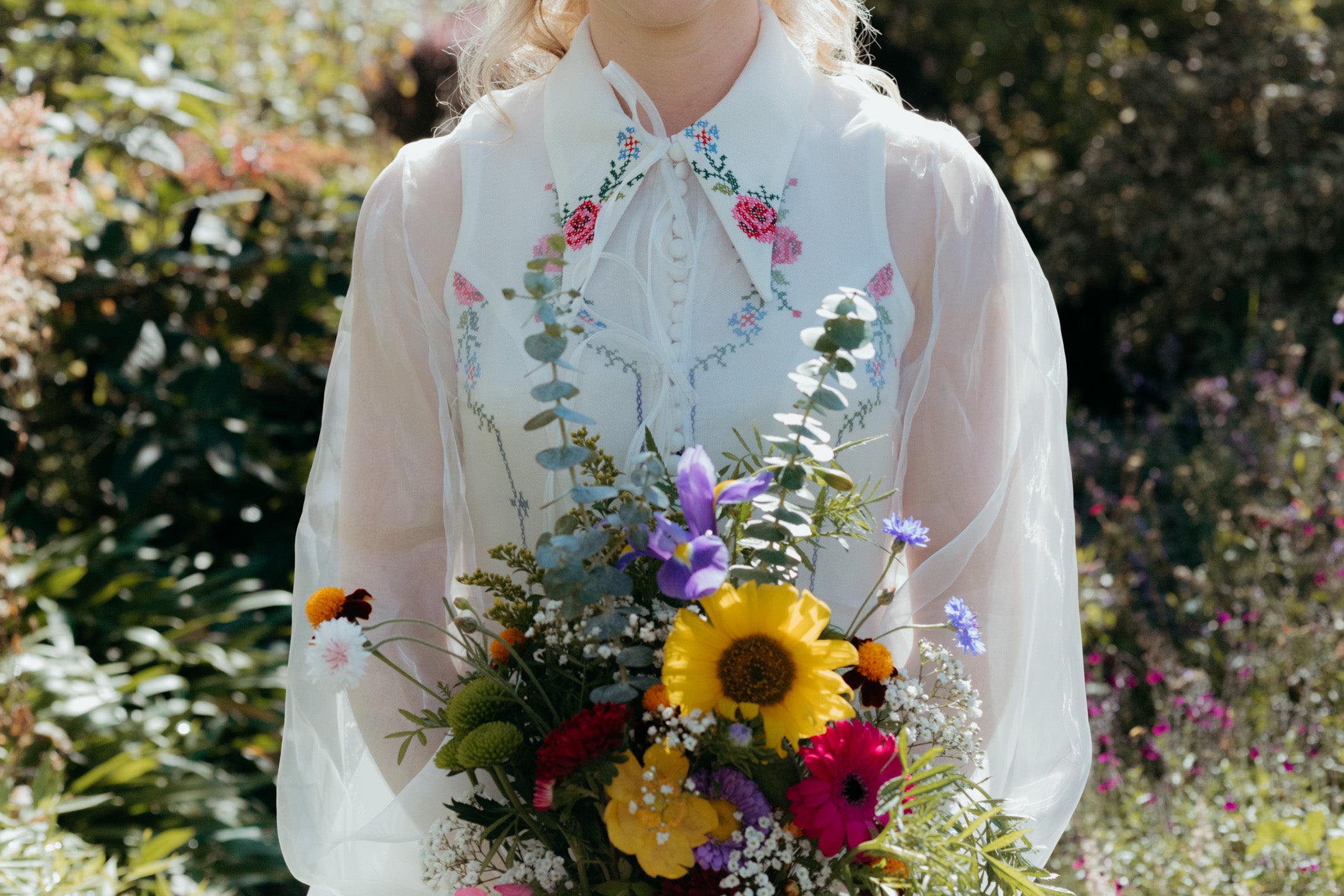 bridal detail close up, shoulders and waist of a person wearing a bridal outfit made from a vintage tablecloth holding a bouquet