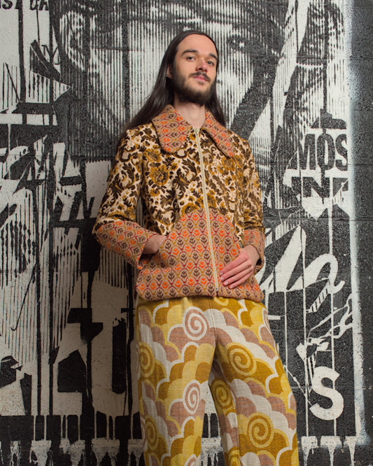 Person wearing a patterned outfit standing in front of a stylized wall design.
